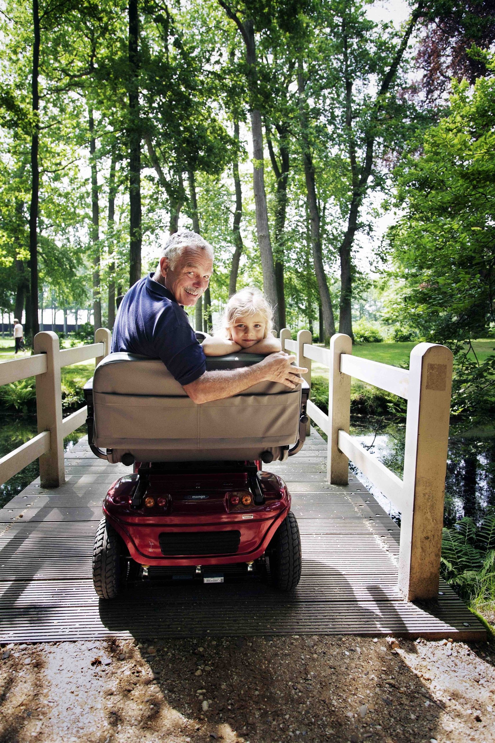 Grandfather on mobility scooter with grandchild on a bridge in the park