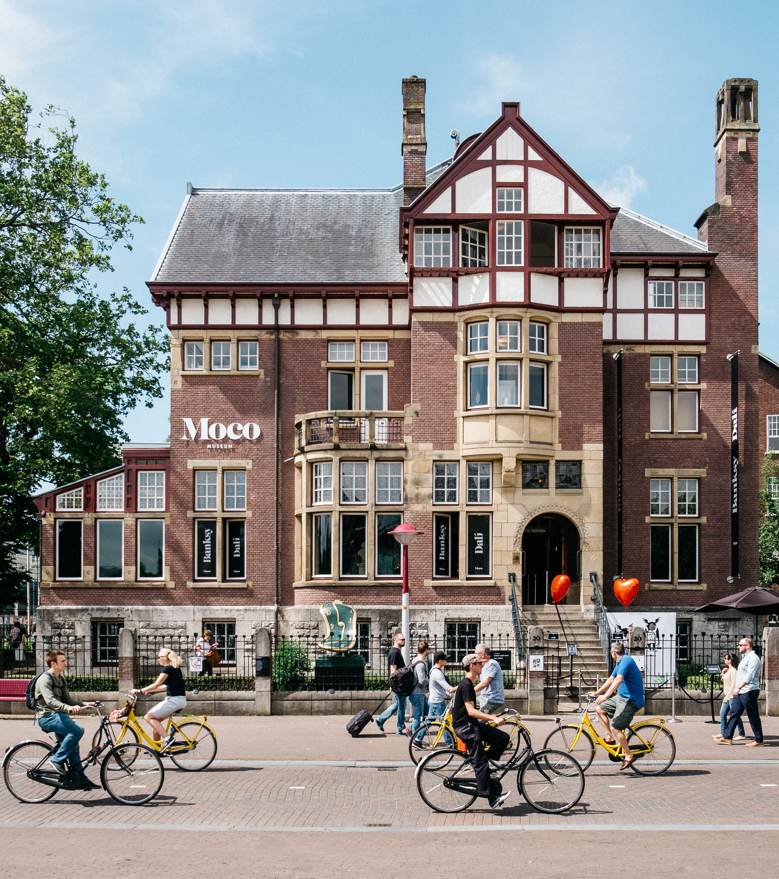 Moco Museum Amsterdam — a historic townhouse on Museumplein with cyclists passing by